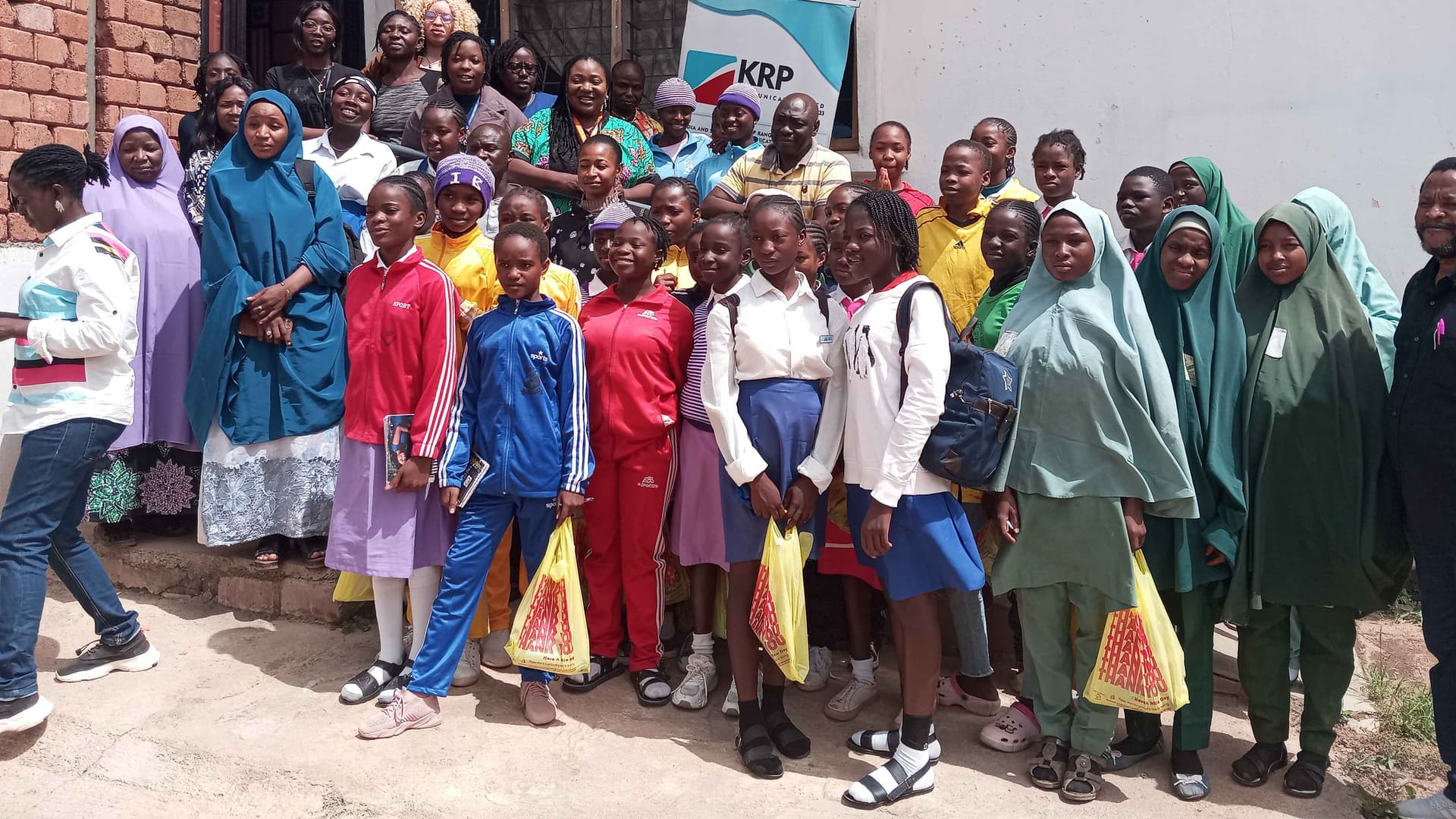 A picture of African girls of high school age as well as African women standing as a group, holding yellow nylon bags. 