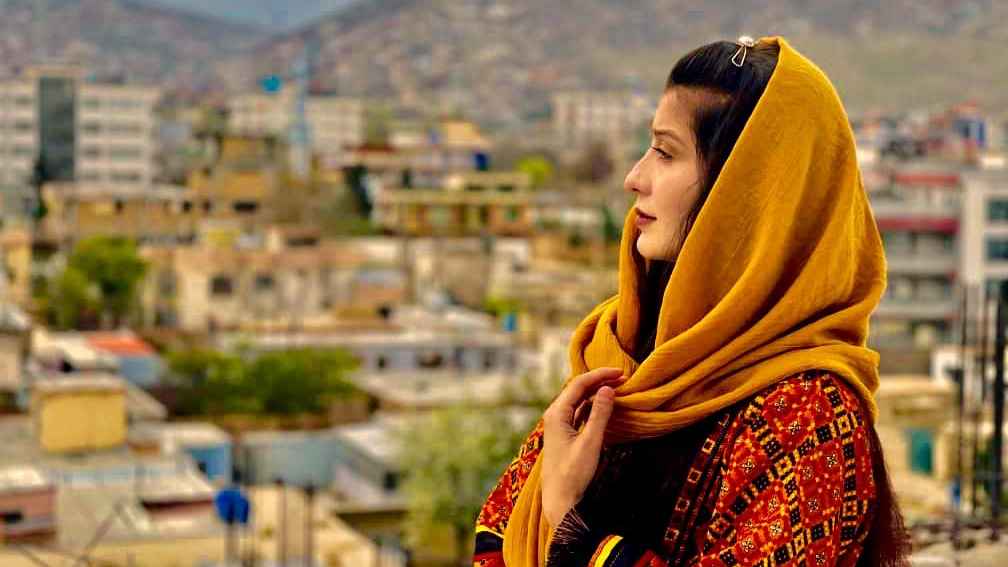 Photo shows a profile view of Maryamsaidi in a yellow headscarf with a city view behind her